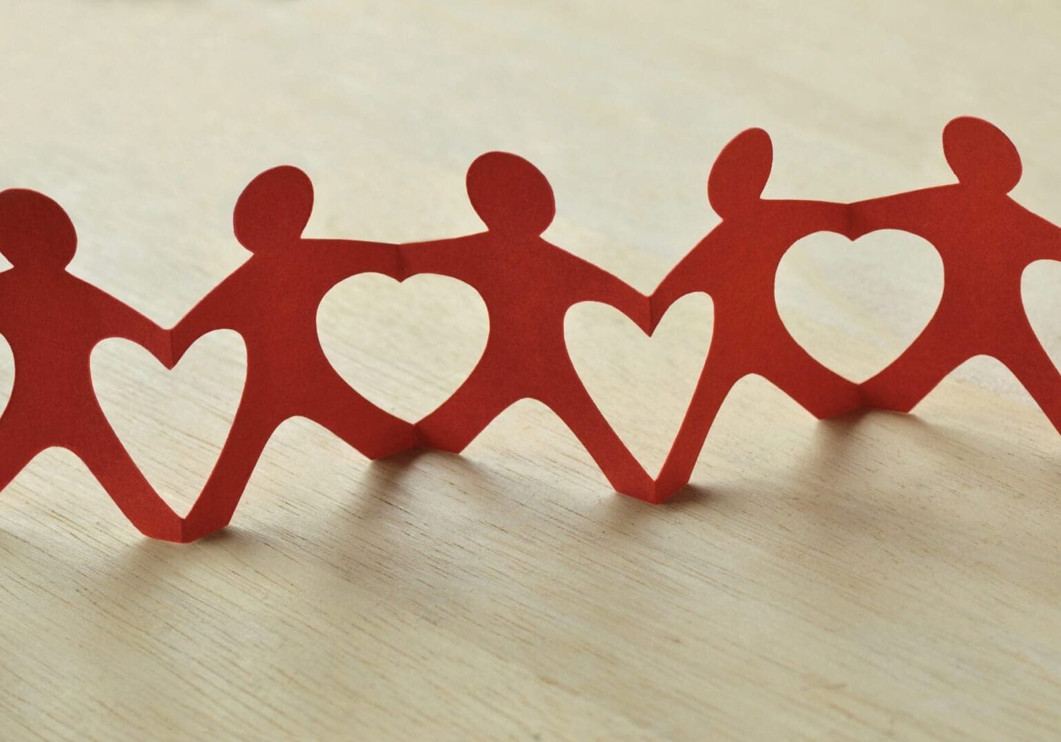 Red paper cutouts of human figures connected by heart shapes, placed on a light wooden surface.
